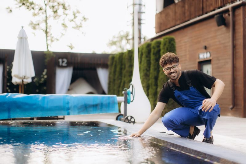 Smiling pool maintenance worker checking water quality by touching the surface of a swimming pool in a luxury hotel resort