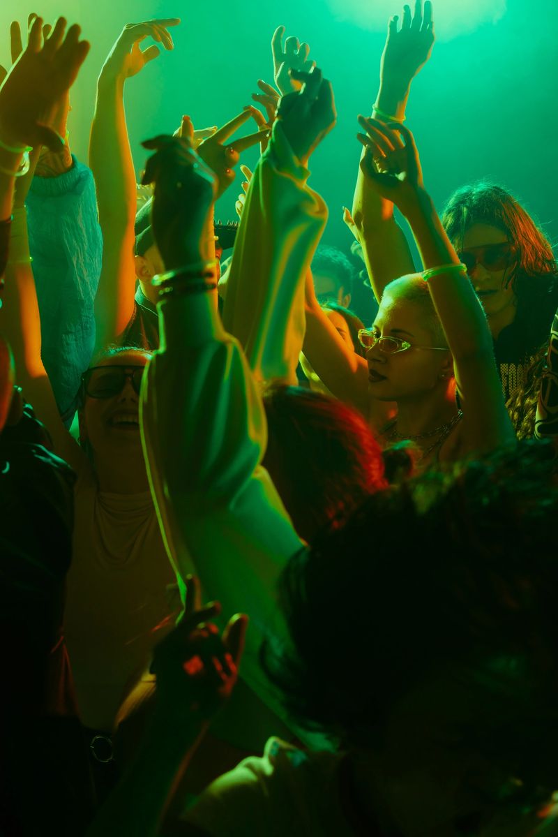 A vibrant, energetic crowd dancing with raised arms under colorful lights at a party or concert. Concept of nightlife, party, youth, summer, festivity, celebration
