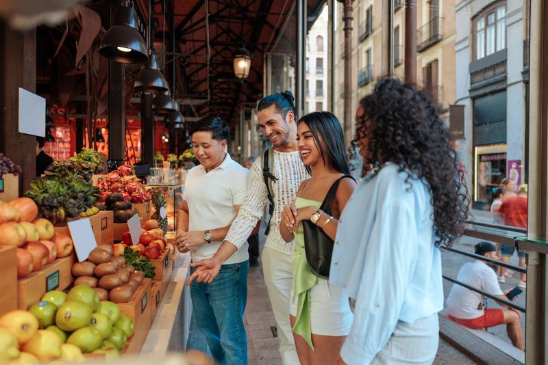 Group of friends buying colorful fresh fruit at a market stall in Mercado de San Miguel, Madrid, Spain