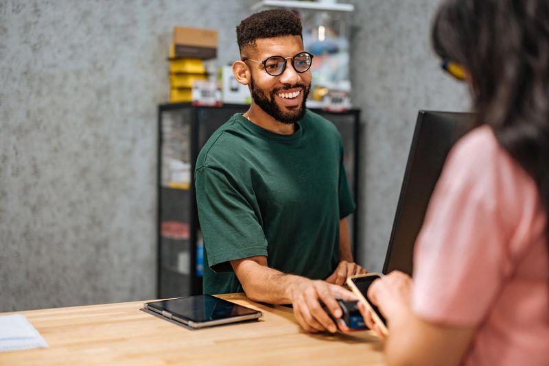 Smiling bicycle shop worker receiving a contactless payment from a customer holding a smartphone over the POS terminal