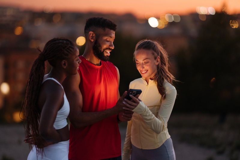 Three friends enjoying a sunset workout, sharing fitness achievements on a smartphone, symbolizing motivation and healthy lifestyle