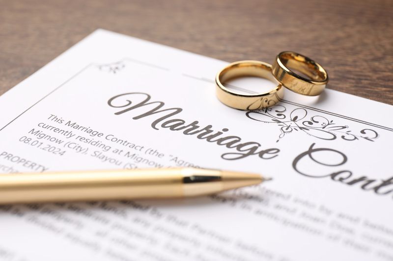 Marriage contract, pen and golden rings on wooden table, closeup