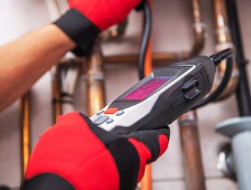 Technician wearing red gloves using a handheld device to inspect copper pipes.