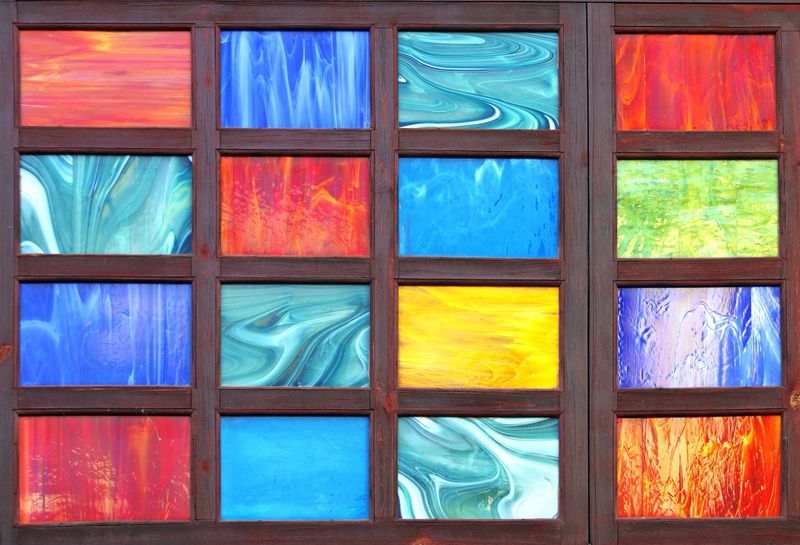 Detail of retro wooden shutter with glass of red, yellow, green and blue colors. Antique wooden shutter, adorned with a glass panel featuring a spectrum of hues. Close-up of vintage wood window frame