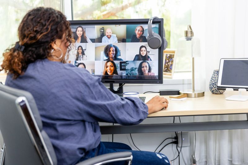 Woman sits at desk, video conferencing with a diverse team.  Home office, technology.