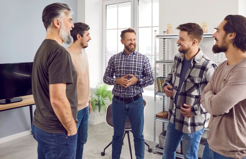 The company of bearded best friends talking and laughing at home standing in a circle. Happy smiling brutal men in casual clothes communicating with each other indoors. Friendship concept.