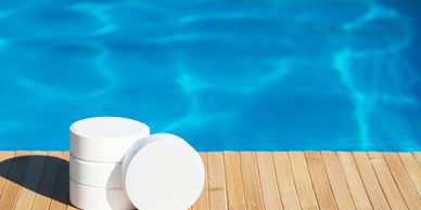 White chlorine tablets stacked near a swimming pool on a wooden deck.