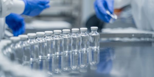 Line of vaccine vials with professionals in blue gloves handling them.