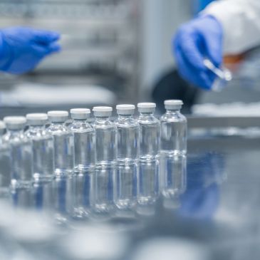 Clear vials lined up in a lab setting with gloved hands.