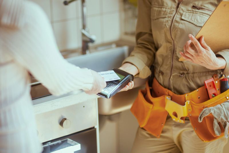 A customer pays a professional for plumbing services with a credit card, finalizing a financial transaction in a home kitchen.