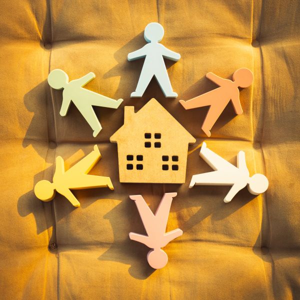 Wooden house figure surrounded by colorful human cutouts on a yellow fabric.