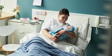 Mother happily holding her newborn in hospital bed.