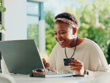 Happy woman shopping online using a credit card at her laptop.