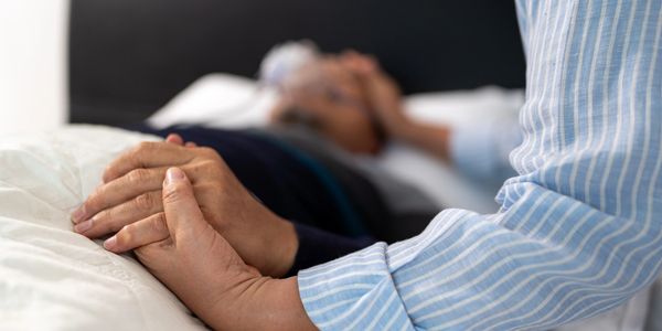 Person holding the hand of a bedridden elderly individual.