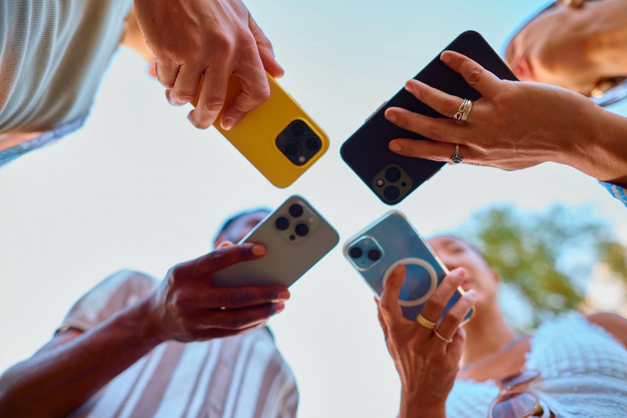 Group of people holding smartphones up in a circle outdoors.