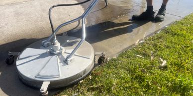 Surface cleaner cleaning a concrete driveway next to grass.