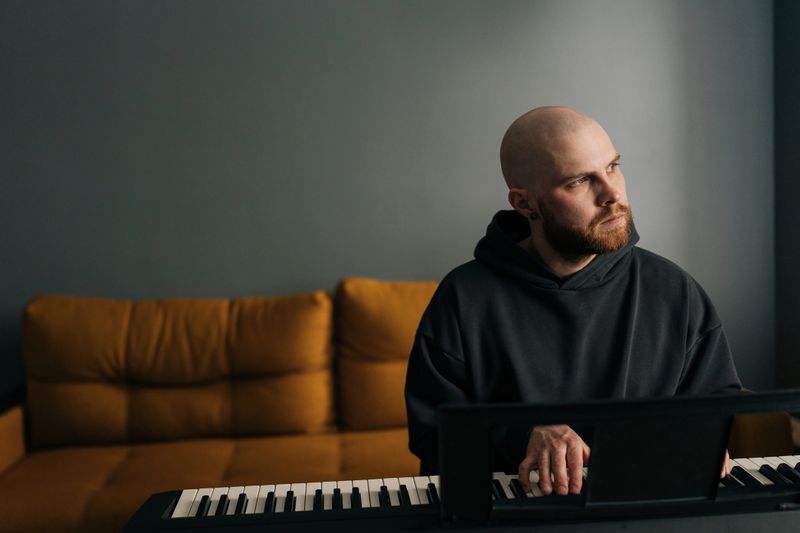 Front view of musician male composing music playing on synthesizer in home studio. Songwriter creating melodic composition, recording new song on electric piano. Concept of recording music at home.