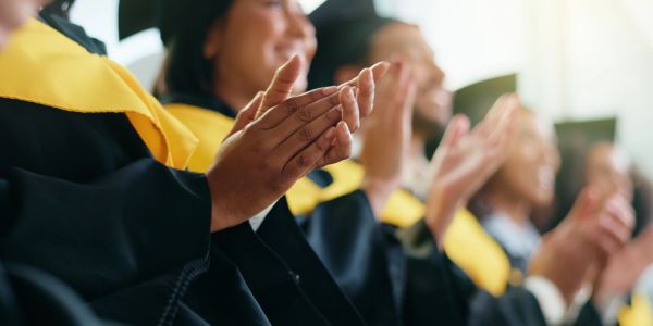 Graduates in caps and gowns applauding joyfully at ceremony.
