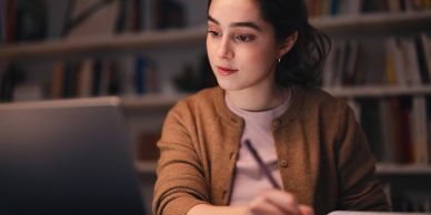 A woman working on a laptop, focused and writing notes. — Admissions Excellence college consulting