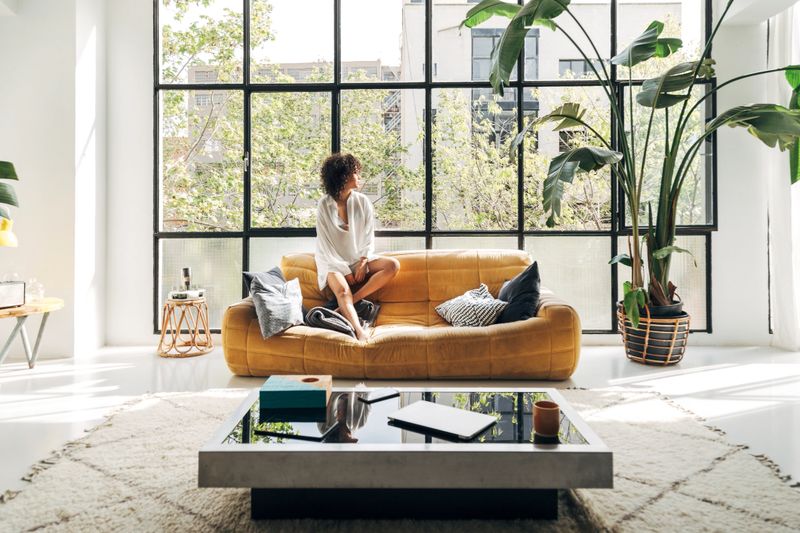 Serene young woman enjoying her bright and airy apartment living room, relaxing on a comfortable sofa amidst modern decor and lush plants