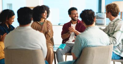 A diverse group of people smiling and sitting in a circle during a meeting.