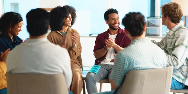 A group of diverse people sitting in a circle and clapping happily.