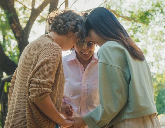 Three people holding hands and smiling outdoors.