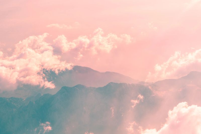 Soft pink clouds gently enveloping rugged mountain peaks create a breathtaking sunset panorama, evoking tranquility and awe in the serene evening atmosphere