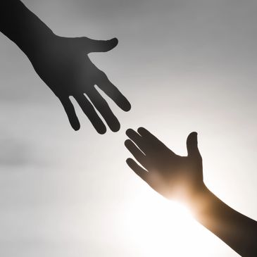 Two hands reaching out to each other against a bright sky.