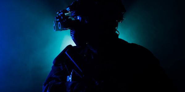 Silhouetted soldier with night vision goggles in blue light.