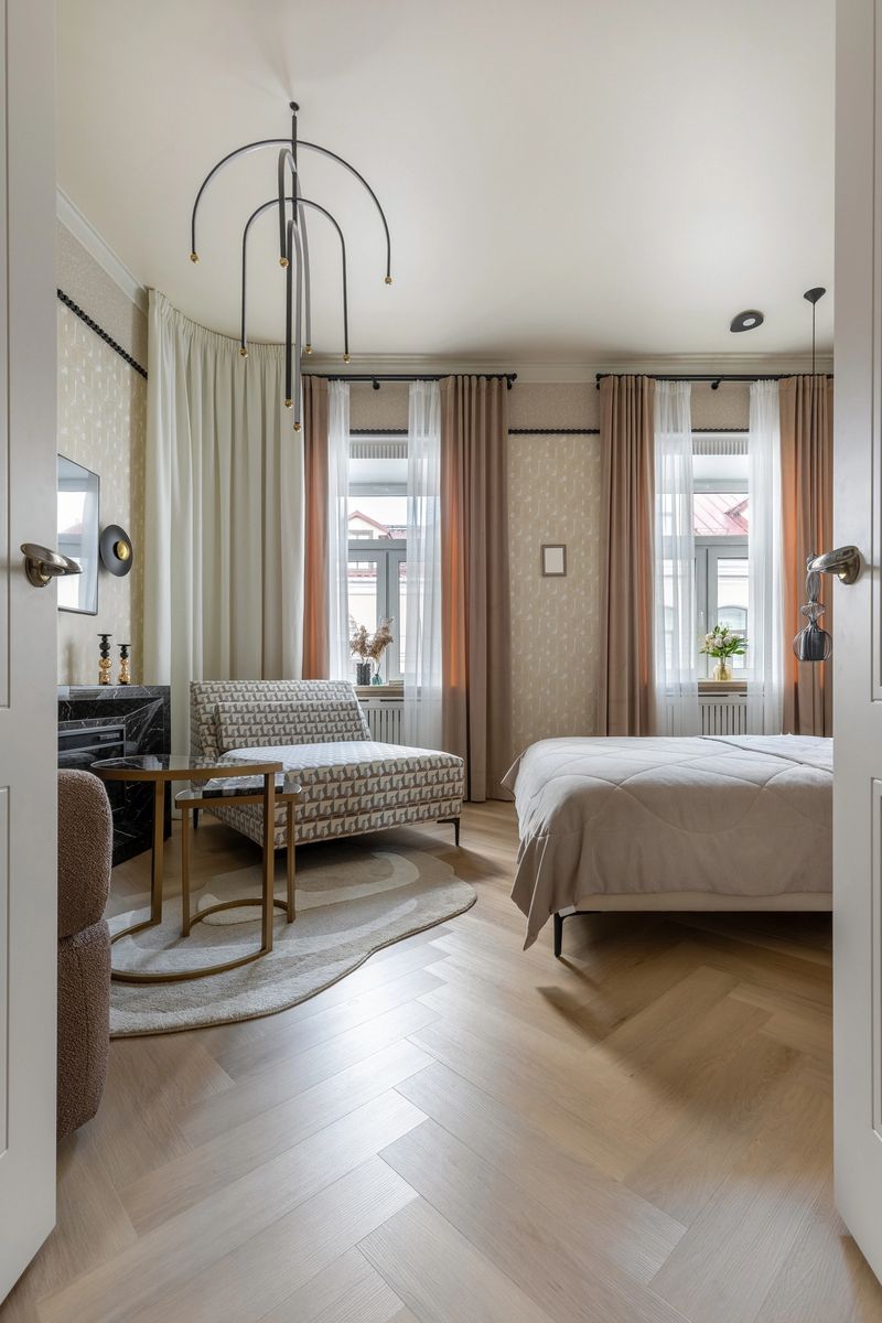 Modern bedroom with geometric furniture, soft curtains, stylish lighting and two large windows letting in natural daylight.