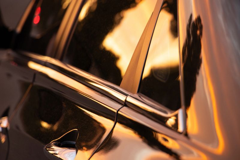 Close-up of a car at sunset, the shine of the body and the reflection of trees and sky on the side door and window, the warm golden light of the evening sun