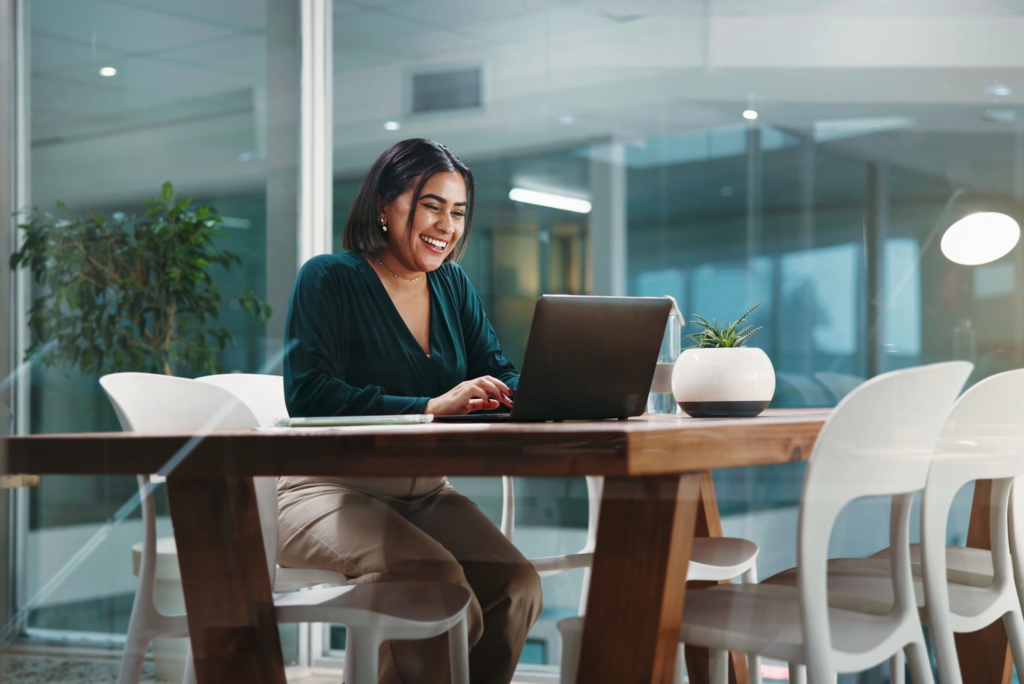 A woman happily working on a laptop in a modern office.