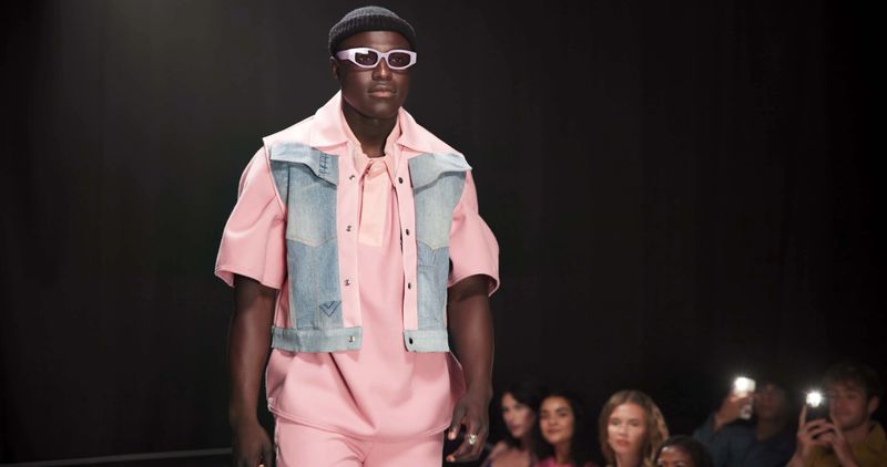 Fashion designer, runway and walking with black man in studio for showcase, clothes presentation and event. Wardrobe launch, luxury brand and collection with model on stage with dark background space