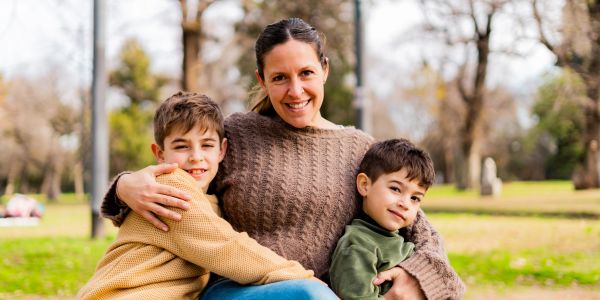 A woman hugging two boys outdoors in a park.