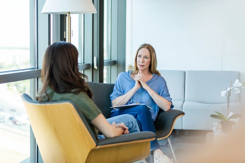 Mature woman therapist listens attentively to a young woman during a session.  Mental health support and care.