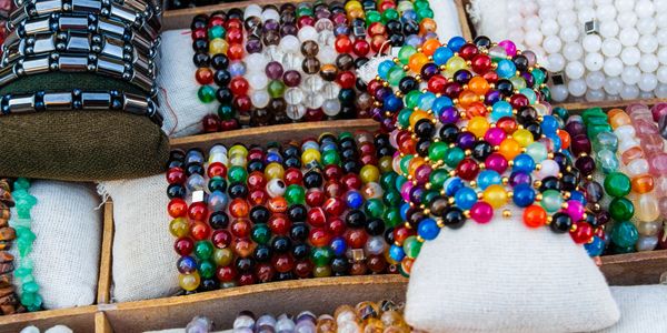 Colorful beaded bracelets displayed on cushions in a wooden tray.