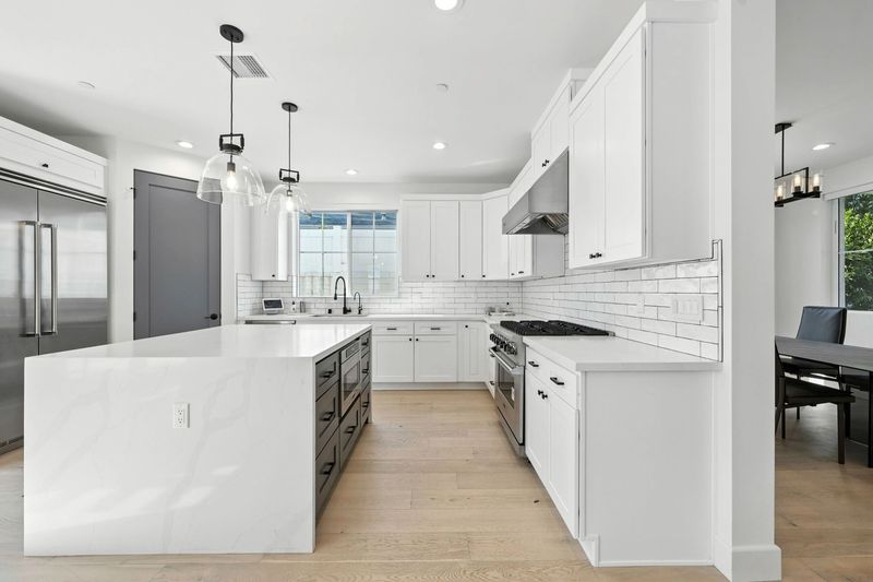 Modern kitchen interior with white cabinetry, large island, stainless steel appliances, and pendant lighting.