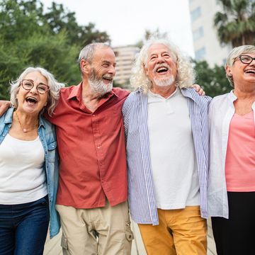 Four elderly friends laughing together outdoors, enjoying each other's company.