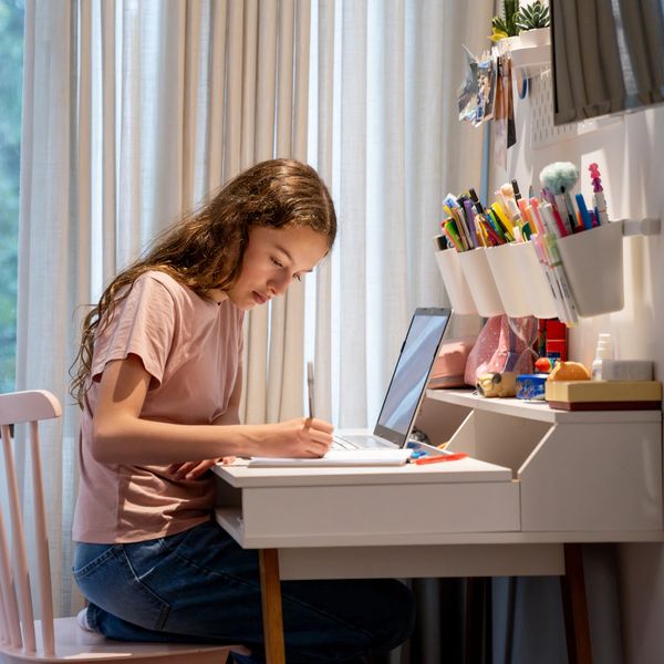 Girl studying at a desk with a laptop and stationery.