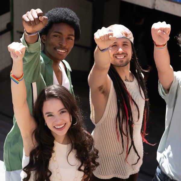 Group of happy diverse friends raising fists together with rainbow bracelets.