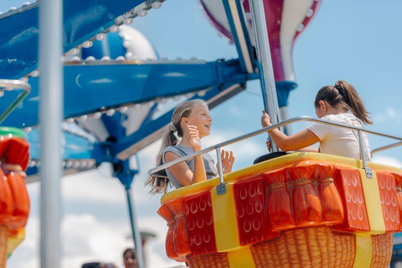 Two young girls enjoying a hot air balloon ride at a summer amusement park, experiencing the joy and excitement of childhood