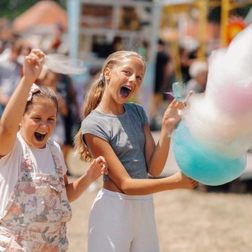Two girls joyfully eating colorful cotton candy outdoors.