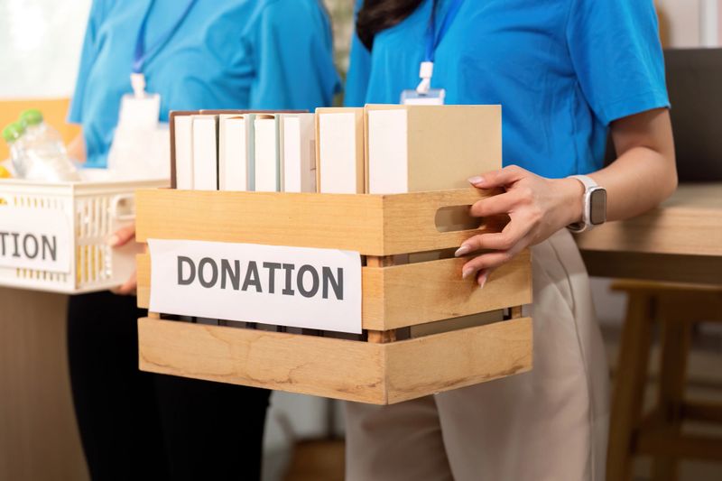 Two volunteers work together, carrying donation boxes filled with essential items, highlighting teamwork and community support.