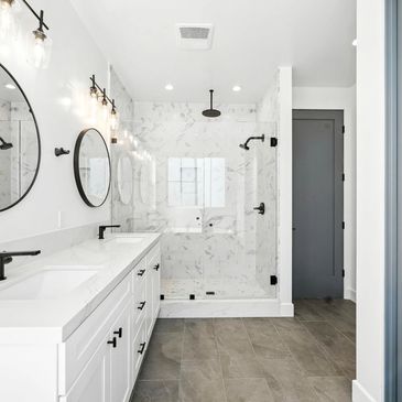 Modern white bathroom with marble shower and dual sinks.