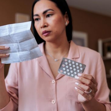 Woman reading medication instructions while holding pills.