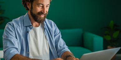 Man with curly hair working on a laptop, smiling.