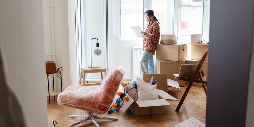 Woman standing in a room with moving boxes and furniture.