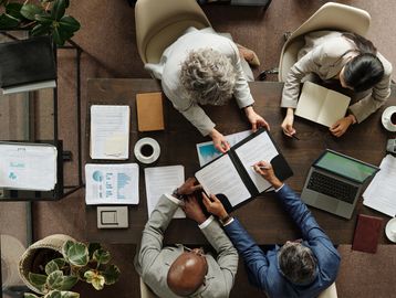 Tres personas en una reunión de negocios con documentos y laptops.