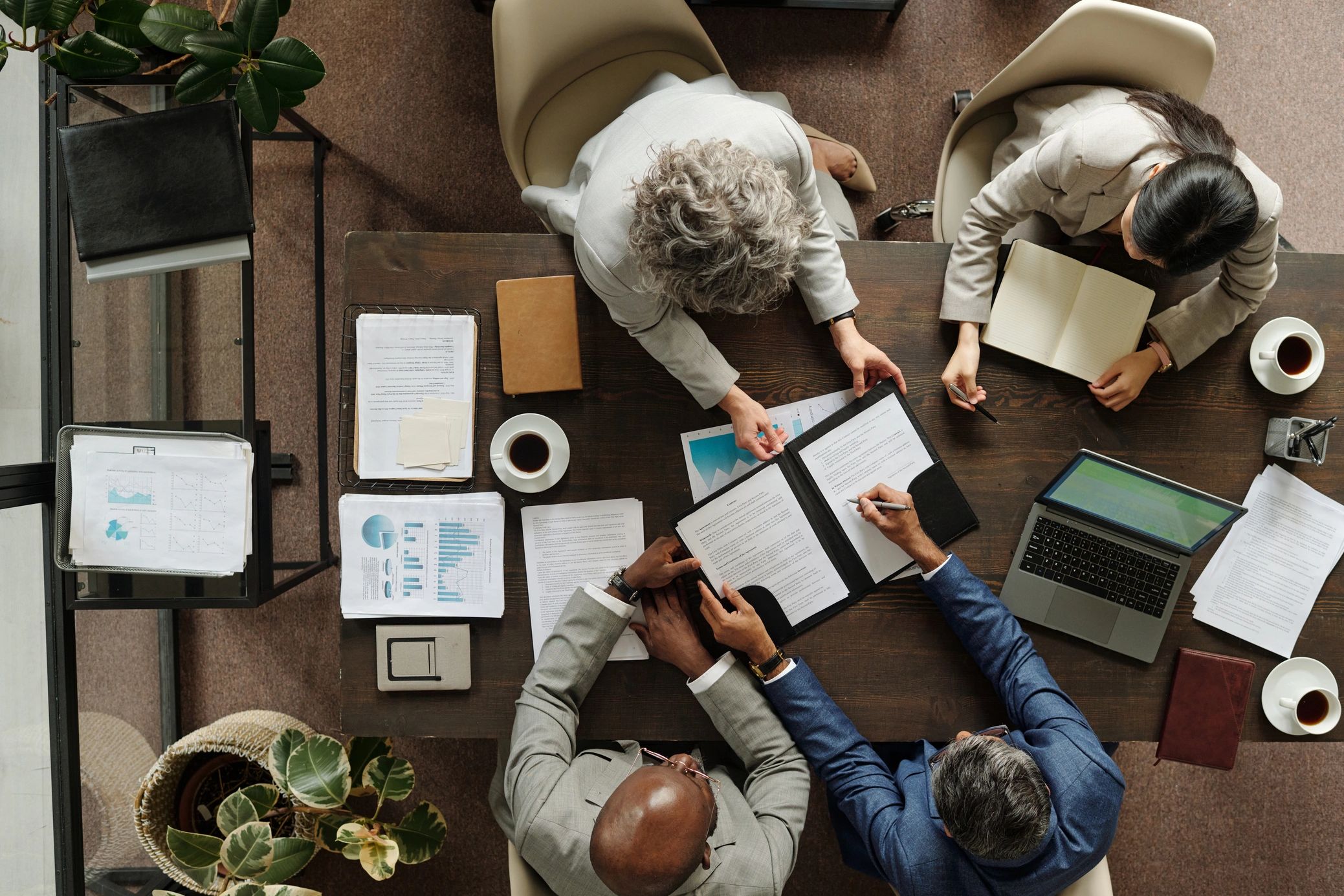 Business team reviewing documents at a table with coffee and laptop.